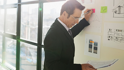 Businessperson wearing a suit going over notes on a whiteboard in sunny conference room
