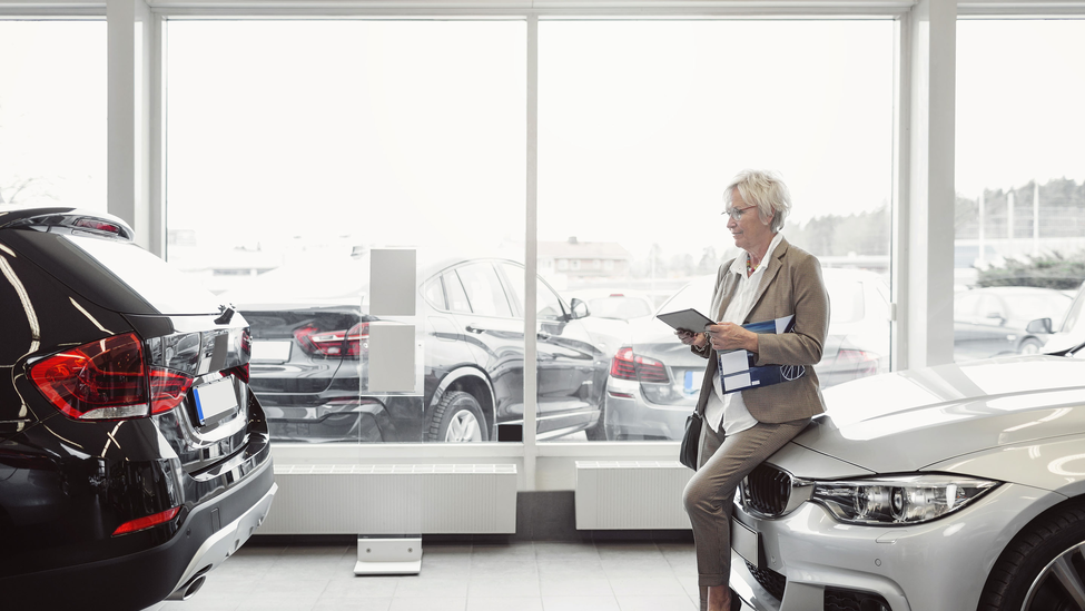 Sales rep leaning against car in dealership lobby.
