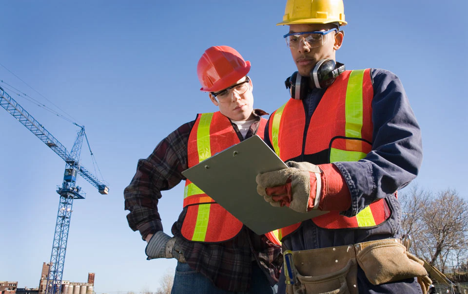 Construction workers on crane site reviewing OSHA standards.